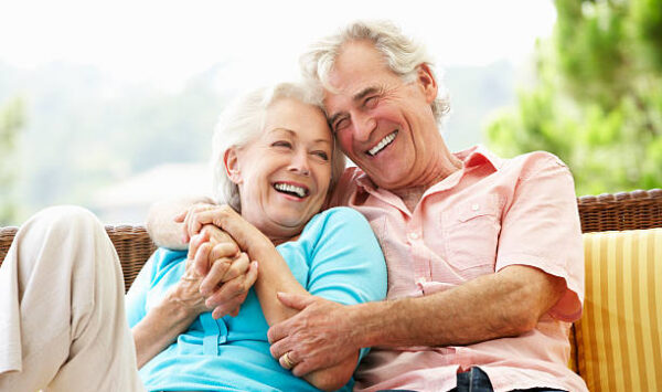 Senior Couple Sitting On Outdoor Seat Together Laughing